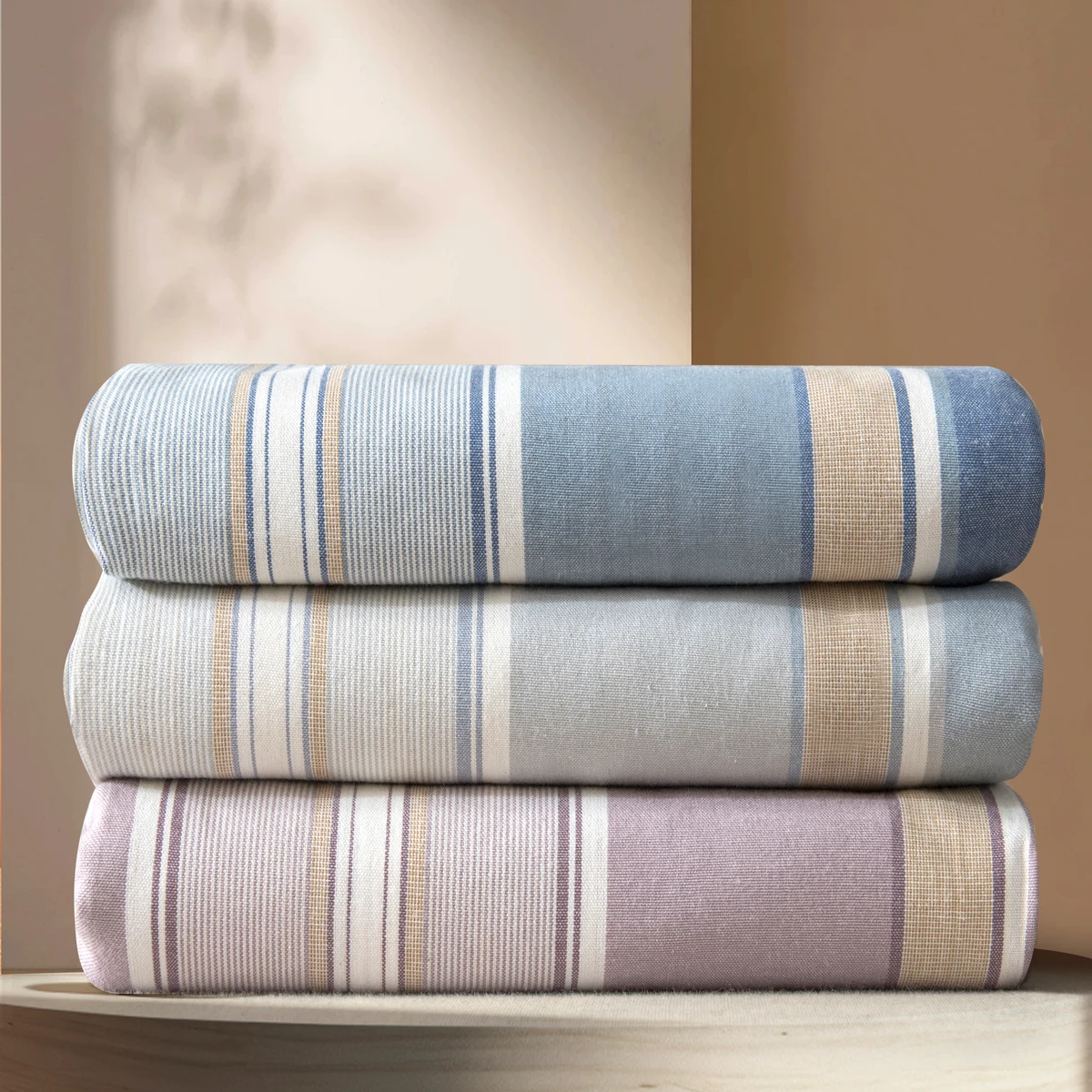 Three folded yarn-dyed cotton fabrics in blue-grey and soft mauve stripes